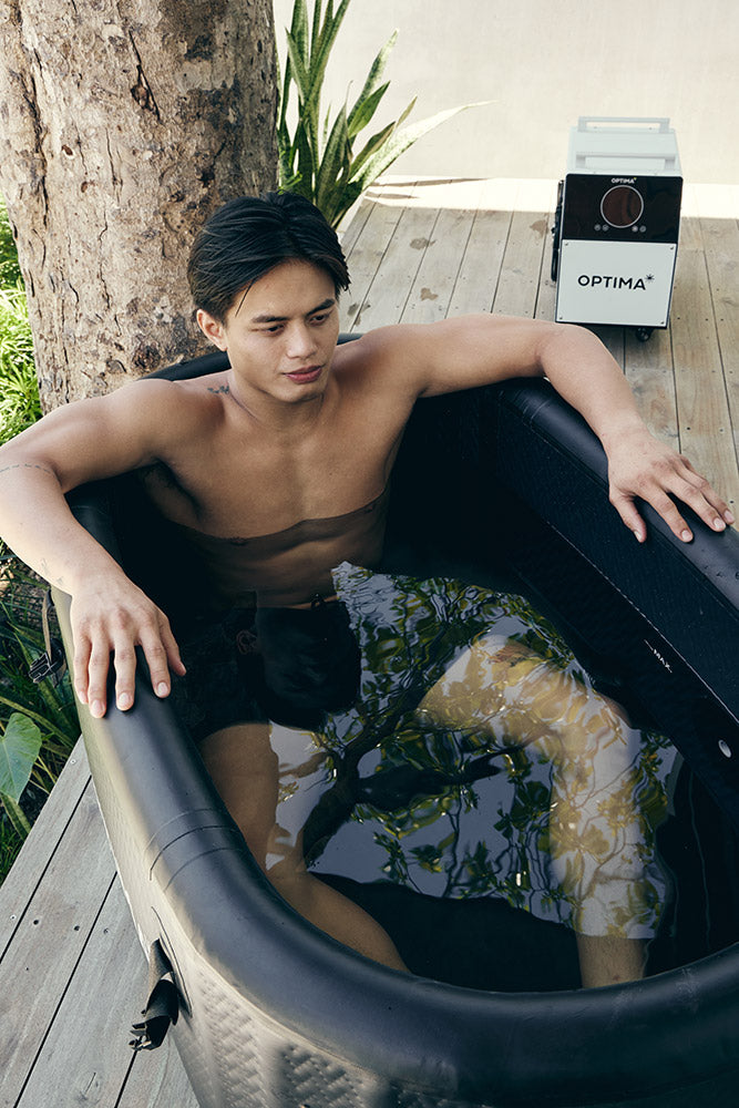 Man sitting in an Optima cold plunge tub outdoors, with the cooling unit in the background.