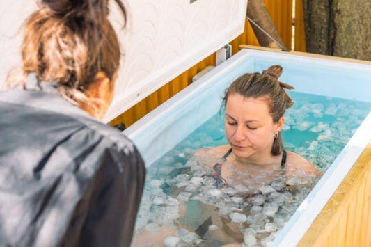 Woman in an ice bath chest freezer with observer beside her.