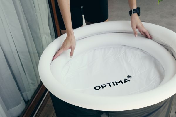 Person assembling an inflatable cold plunge tub labeled "OPTIMA".
