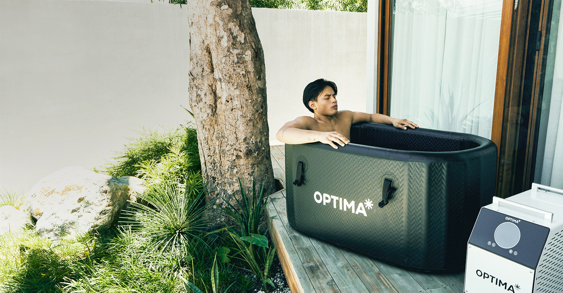 Man sitting in a Optima Tub Plus ice bath on a wooden deck. 